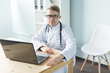 Fototapeta premium Healthcare, medical and people concept - Young caucasian doctor sitting in his office and smiling
