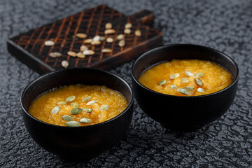 Roasted pumpkin soup with pumpkin seeds on dark concrete background.