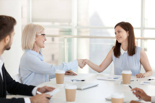 Happy millennial employee shake hand of mature colleague getting acquainted at meeting, diverse coworkers handshake greeting at briefing, introducing in boardroom or congratulating with promotion