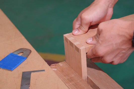 Skilled joiner working in carpentry. Amateur woodworker making dovetail join for wooden drawer in carpenters workshop