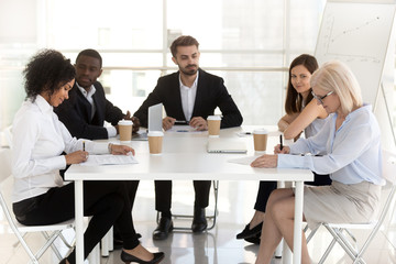 Excited diverse employees watch new workers sign contract at business meeting in office, female...