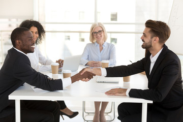 Smiling diverse business partners shake hand closing deal at office meeting, multiethnic excited businessmen handshake making agreement, starting cooperation after successful negotiation