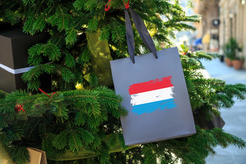 Luxembourg flag printed on a Christmas shopping bag. Close up of a shopping bag as a decoration on a Xmas tree on a street. New Year or Christmas shopping, local market sale and deals concept.  © theartofpics