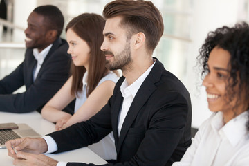 Diverse millennial employee sit in row at table looking at presenter or job candidate smiling, multiethnic workers like speaker or applicant, impressed recruiters feel positive at interview - obrazy, fototapety, plakaty