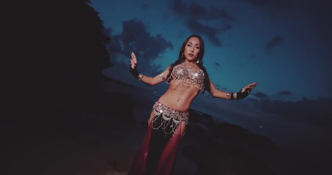 Beautiful tribal belly dancer outdoors. Woman in oriental costume dancing near the sea during sunset