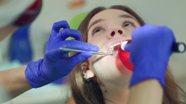 Close up woman patient with open mouth at dental procedure. Dentist working with dental polymerization lamp in oral cavity. Dental treatment in teeth care centre