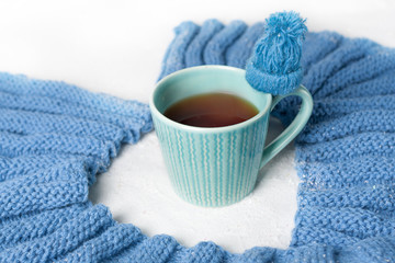 Winter concept.  Blue white color . A cup of hot tea with knitted texture flavored with a  knitted scarf and little hat on white backgroung. Cold color.
