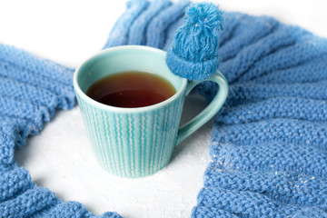 Winter concept.  Blue white color . A cup of hot tea with knitted texture flavored with a  knitted scarf and little hat on white backgroung. Cold color.