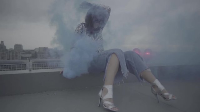 Cute woman with smoke bomb over city background. Slow motion, s-log, ungraded
