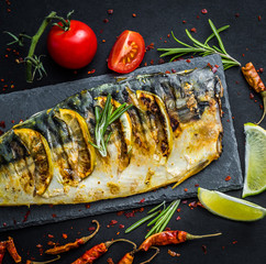 Grilled mackerel fillets with lime on black slate board, fish with vegetables and herbs