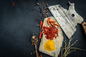 Colourful spices and herbs with old kitchen ax on a black table