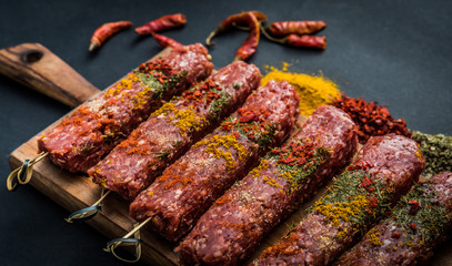 Raw kebab with spices on a black table