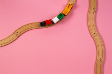 Toy train and wooden rails on pink color background