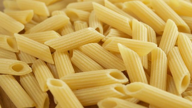 dry italian Penne pasta on rotate on wood background