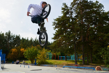 Full length portrait of modern young man doing stunts on bmx bike jumping high over ramps in...