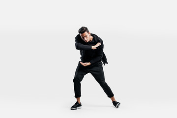 Dark-haired stylish man dressed in a stylish black clothes is dancing street dance. He makes stylized movements with his hands