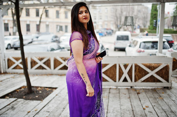 Indian hindu girl at traditional violet saree posed at street against wooden terrace.