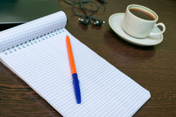 a clean notebook on the desktop, next to the laptop, a cup of coffee, headphones. A place to create ideas