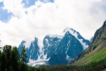Fototapeta premium Snowy mountain top between rocky mountains under overcast sky. Rocky ridge in mist above forest. Atmospheric minimalistic landscape of majestic nature.