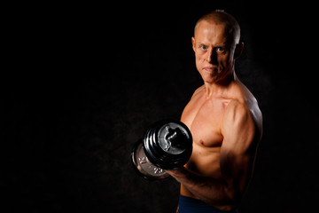 Fototapeta na wymiar Fit muscular man exercising with dumbbell on dark background