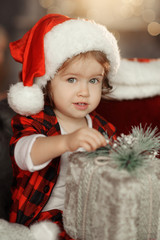 Christmas cute toddler girl in Santa hat holding a a gift box. Family holiday concept.