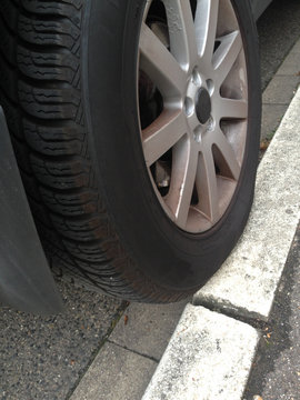 Auto parkt nur halb auf der Bordsteinkante, der Reifen rutscht langsam ab