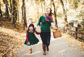 Fototapeta premium A young mother with a toddler daughter running in forest in autumn nature.