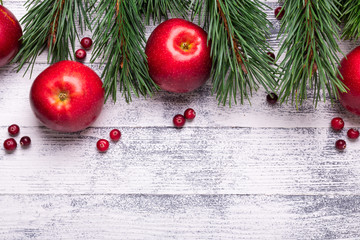 Christmas background with tree branches, red apples and cranberries. Light wooden table