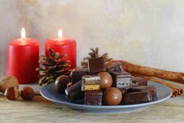 filled gingerbread cookies, in germany called domino steine, chocolate balls and red candles for Advent and Christmas on a rustic wooden table, copy space