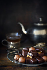christmas chocolate sweets on a plate, silver teapot and cup blurry in the dark rustic background with copy space, vertica