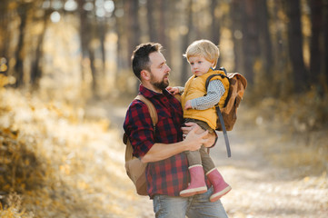 Fototapeta premium A mature father holding a toddler son in an autumn forest, talking.