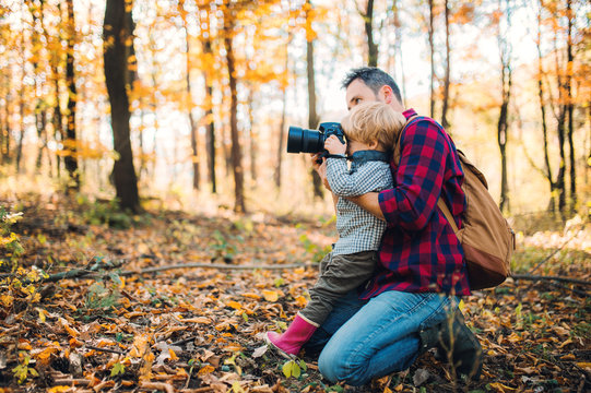 A mature father and a toddler son in an autumn forest, taking pictures with a camera.