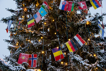 Christmas tree with lights and covered in snow. Instead of decorative elements, flags are showing the international approach of celebrating Christmas.