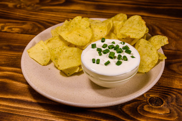 Ceramic plate with potato chips and glass bowl with sour cream on wooden table