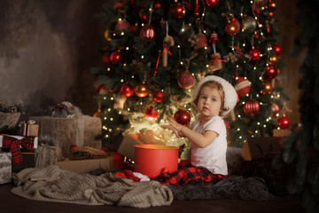 Happy little smiling girl in red pajamas and Santa hat with christmas gift box in the living room...