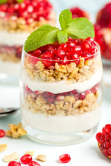 Pomegranate parfait - sweet organic layered dessert with granola flakes, yogurt and red ripe fruit seeds.