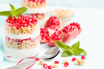 Pomegranate parfait - sweet organic layered dessert with granola flakes, yogurt and red ripe fruit seeds.