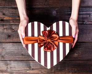 female hand holding a striped handmade box with a bow on wooden background © Masson