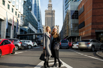 two beautiful women stand in the center of the city and smile in the warm autumn