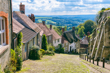 Bright scenic landscape view of the rolling green countryside from the cobblestone street of a traditional English village - 231956862