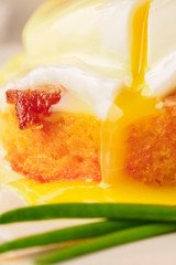 Breakfast is Eggs Benedict - toasted English muffins, bacon, ham, poached eggs, herbs and delicious buttery hollandaise sauce. Close-up of drop of liquid egg yolk.