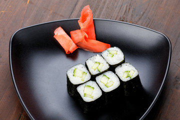 Vegetarian sushi with cucumber. Set sushi rolls with ginger on a black plate on a dark wooden background.
