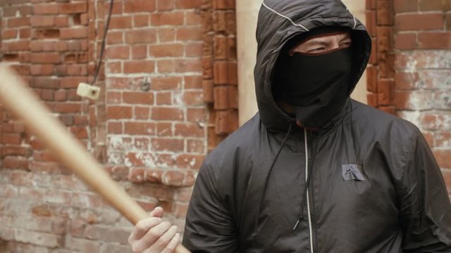 Portrait of bandit with mask and baseball bat on brick wall background .