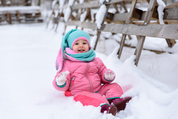 little girl in a pink jumpsuit walks in a snowy winter park