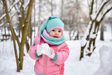 little girl in a pink jumpsuit walks in a snowy winter park