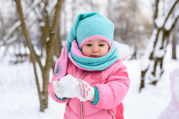 Fototapeta na wymiar little girl in a pink jumpsuit walks in a snowy winter park