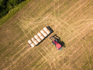 Aerial Drone Photo of Farmer Harvesting Hay Rolls in the Wheat Field with a Red Tractor