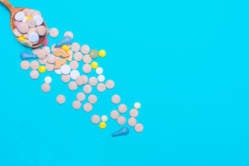 Assorted pharmaceutical medicine pills, tablets and capsules on wooden spoon on blue background.