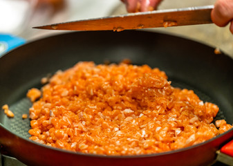 Red Pan with Pile of Cutted Salmon Pieces in the Foreground, Male Chef Cutting Fresh Salmon on the Wooden Board in the Background