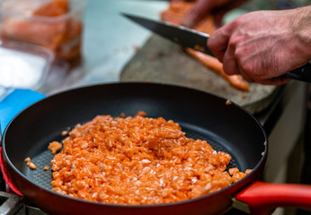 Red Pan with Pile of Cutted Salmon Pieces in the Foreground, Male Chef Cutting Fresh Salmon on the Wooden Board in the Background